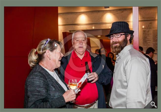 Three people are engaged in a cheerful conversation while holding drinks at an event.