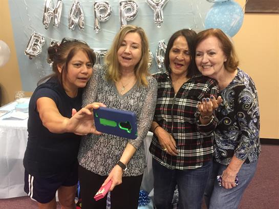 Friends gather for a birthday celebration, smiling and taking selfies together at the event.