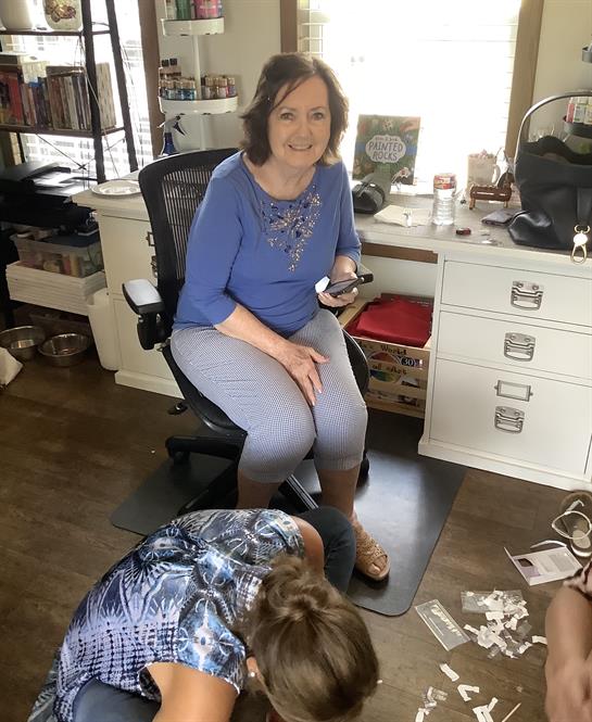 A woman relaxes in an office chair with her phone as someone organizes papers nearby.