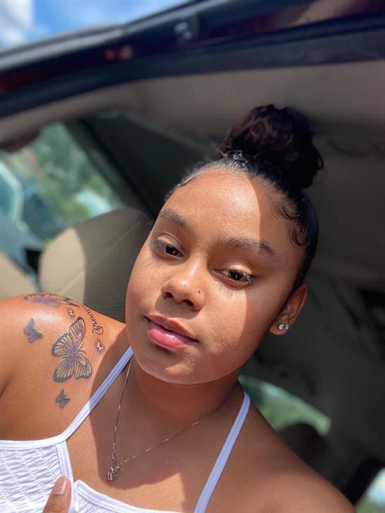 A woman with a bun hairstyle and tattoos enjoys the sunshine while sitting in a car.