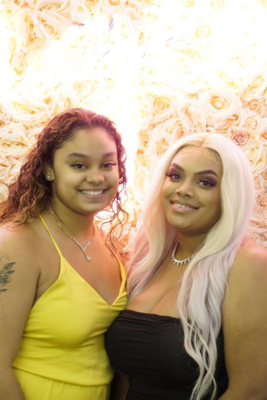 Two friends pose happily together in front of a vibrant backdrop during a lively celebration.