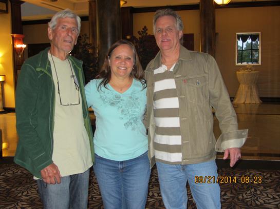 Three people are smiling together in a welcoming lobby during a friendly gathering.