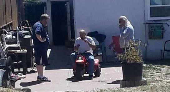 One man enjoys riding a small red vehicle while two others observe and chat nearby.