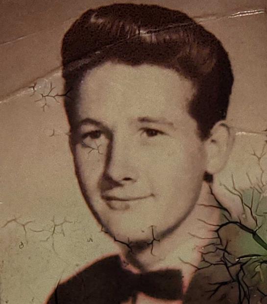A young man with slicked-back hair smiles confidently in a nostalgic vintage portrait.