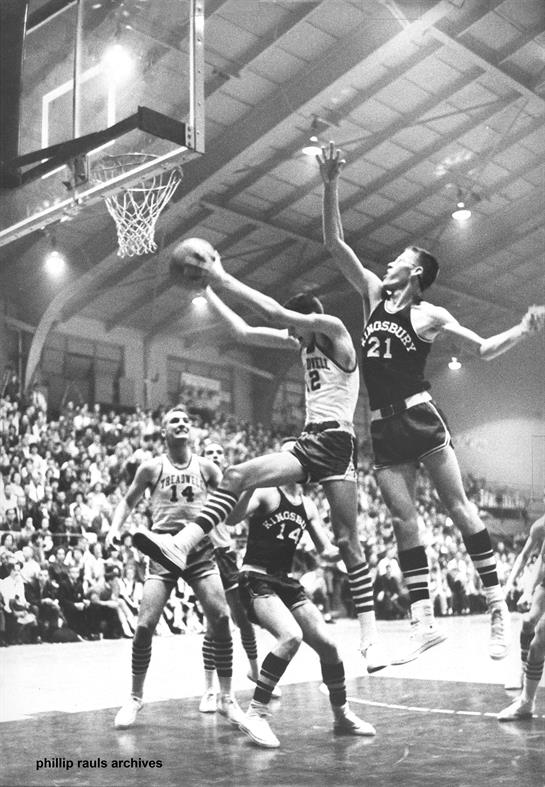 Two basketball players battle for a shot in a lively arena filled with fans.