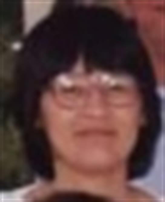 A woman with glasses smiling warmly while surrounded by family members outdoors.