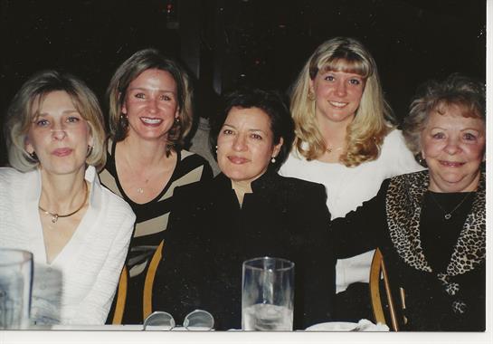 Five women are smiling and posing together at a restaurant table during a lively dinner gathering.