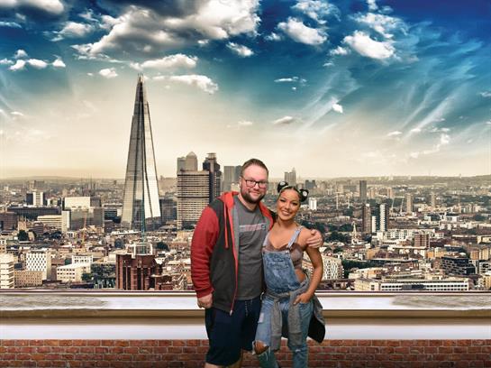 A couple stands together on a rooftop, taking in the stunning urban landscape at sunset.