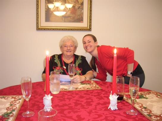 Two women smile together at a festive table adorned with candles and sparkling glasses.