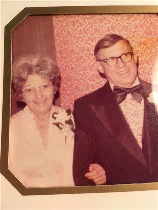 A happy couple enjoys their anniversary at a formal gathering, dressed elegantly and smiling.