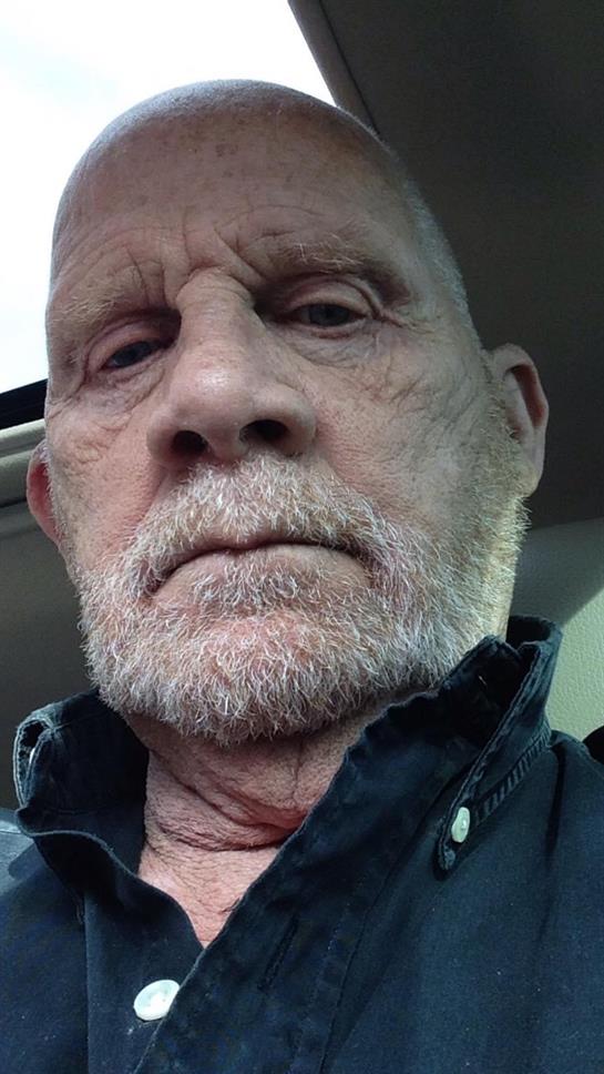 Elderly man with a gray beard poses for a selfie inside a car, sunlight entering from the window.