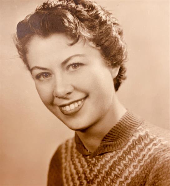 Woman with curly hair smiles warmly, wearing a patterned sweater in a vintage setting.