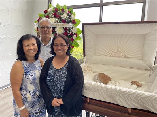 Friends and family gather in remembrance, standing beside a casket adorned with flowers.