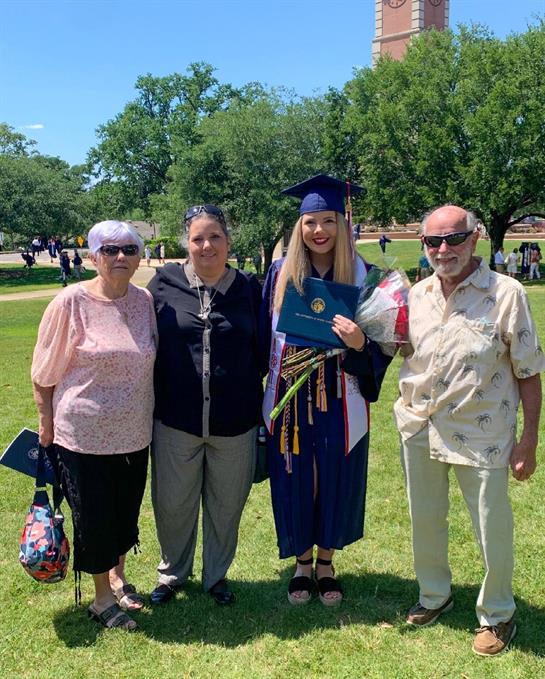 Family gathers in a park to celebrate a graduation ceremony under sunny skies.