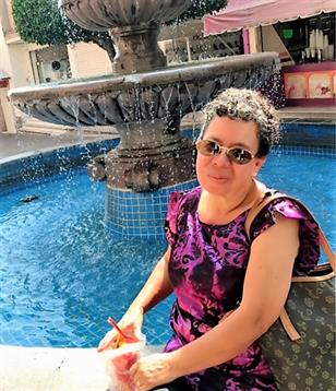 Woman enjoys a moment by a beautiful fountain, sketching in a vibrant plaza with colorful shops.