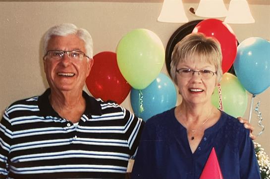 Happy couple stands together in a decorated room filled with vibrant balloons and smiles.