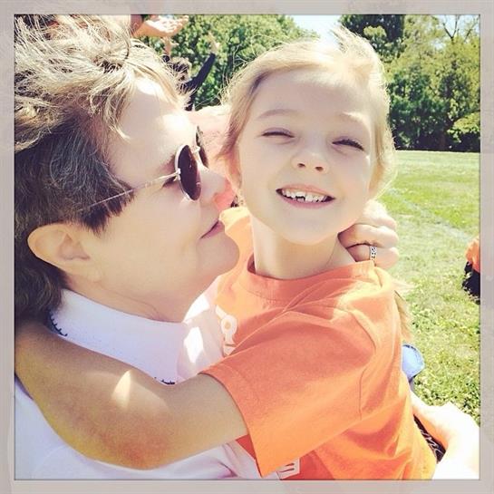 A joyful child hugs an adult, both sharing a loving moment outdoors on a sunny day.