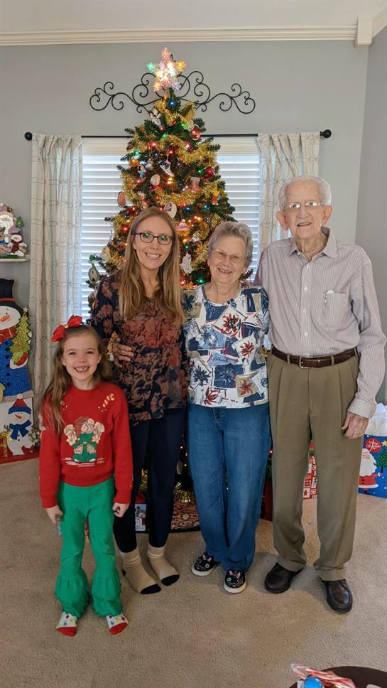 A joyful family stands together, smiling in front of a decorated Christmas tree and gifts.