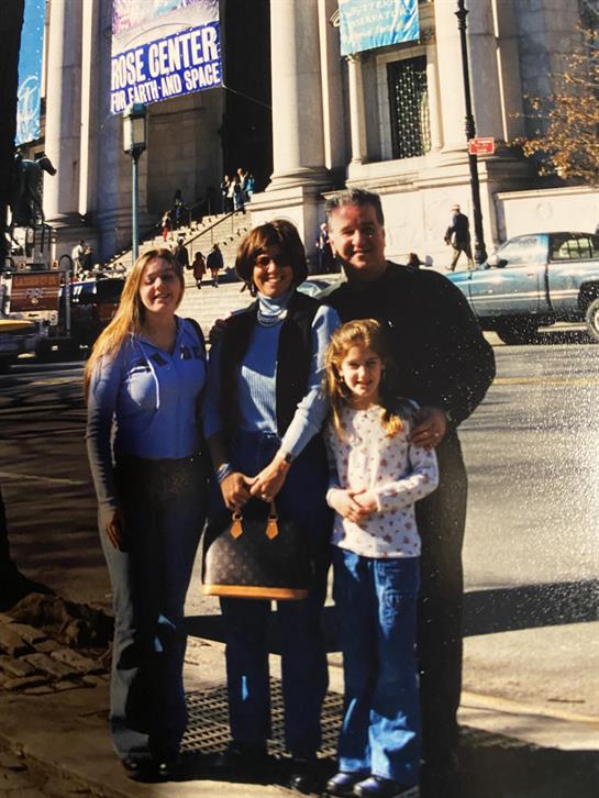 Four family members pose happily in front of a grand museum on a sunny day, smiling together.