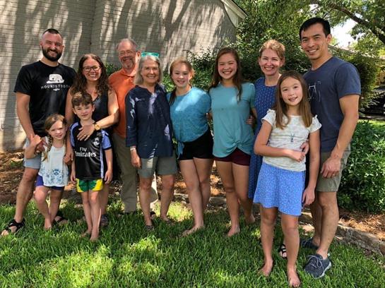 A diverse group of adults and children gather outdoors, sharing smiles and laughter.