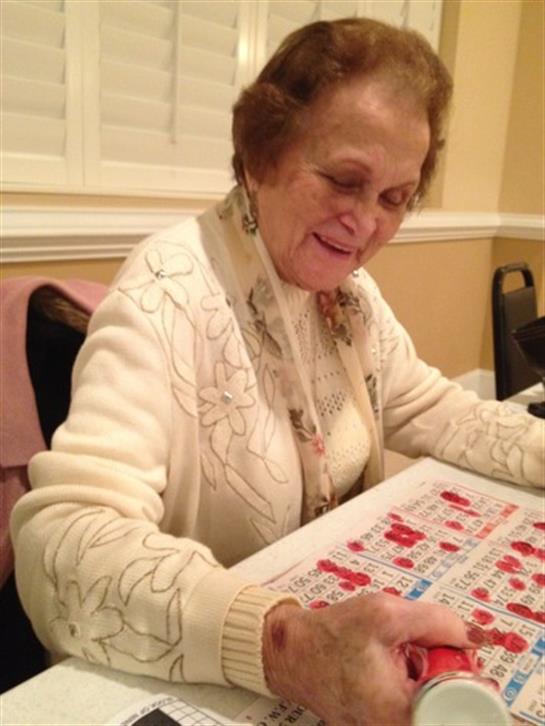 Smiling senior woman plays bingo at a community center surrounded by friends during the evening.