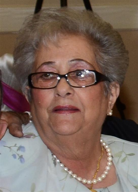 A cheerful elderly woman with glasses and pearls enjoys a family gathering in a cozy setting.
