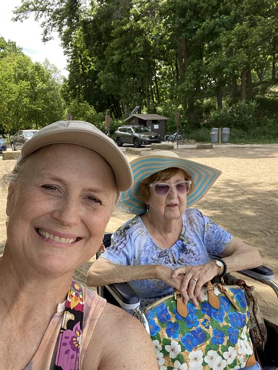 Two women smile and relax at a park, enjoying a sunny day and each other's company while resting.