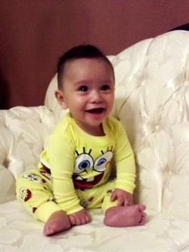 A happy baby laughs on a soft couch in a cheerful yellow outfit with a cartoon.