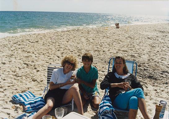 Three family members relax on beach chairs, enjoying snacks and the warm sunshine on the sand.