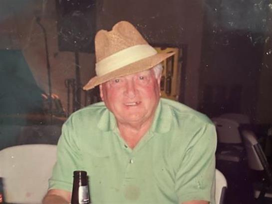 Man wearing a straw hat smiles while holding a drink in a relaxed setting.