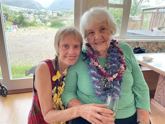 Joyful women in colorful leis share a drink in a bright room.