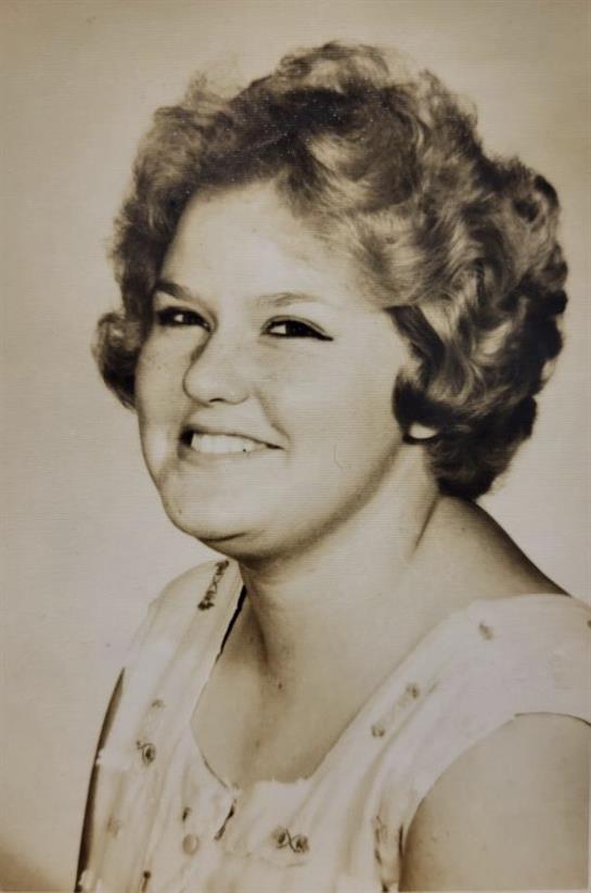 A cheerful woman with curly hair smiles warmly, capturing a nostalgic moment from the past.