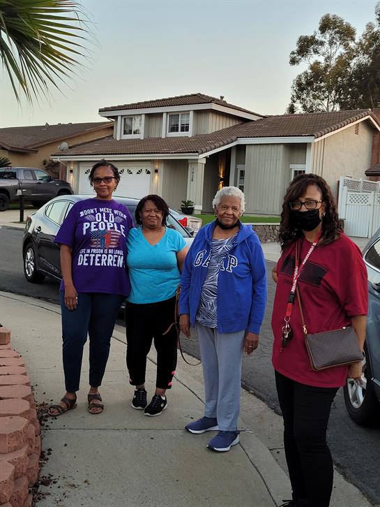 Four women gather in a suburban area, smiling and enjoying each other's company in the evening.