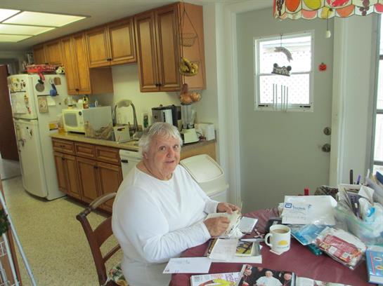 An elderly person sorts through photos at a sunlit kitchen table.