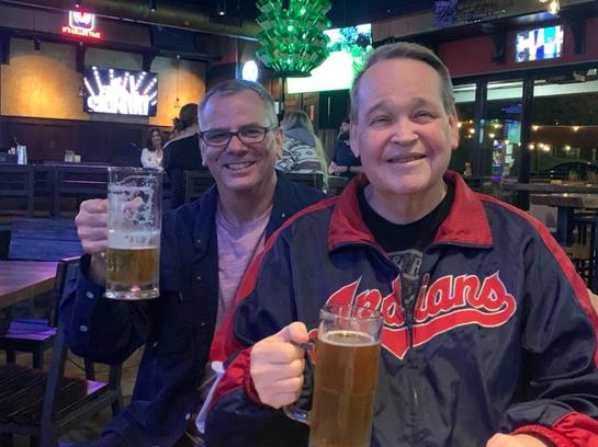 Friends raise their drinks in celebration at a busy bar filled with lights and laughter.
