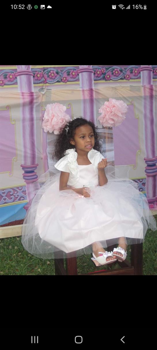Young girl wearing a beautiful white dress sits gracefully among party decorations.