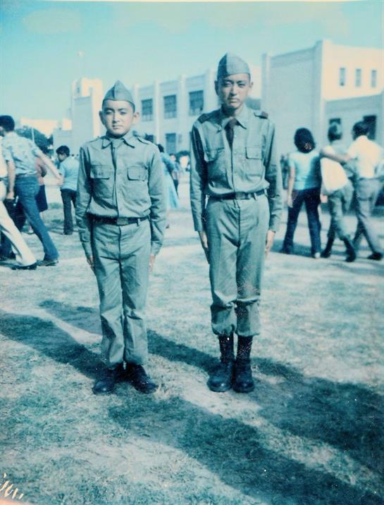Two young cadets stand in formation during a training event in a sunny outdoor setting.