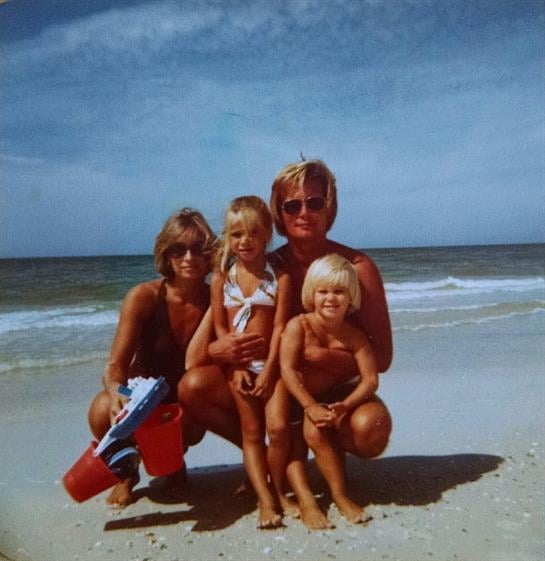 Family poses on the sandy beach while children play and enjoy the warm weather by the sea.