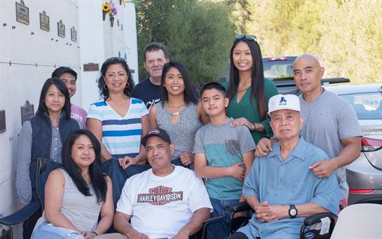 A group of family members poses together, smiling happily, enjoying a sunny day outdoors.