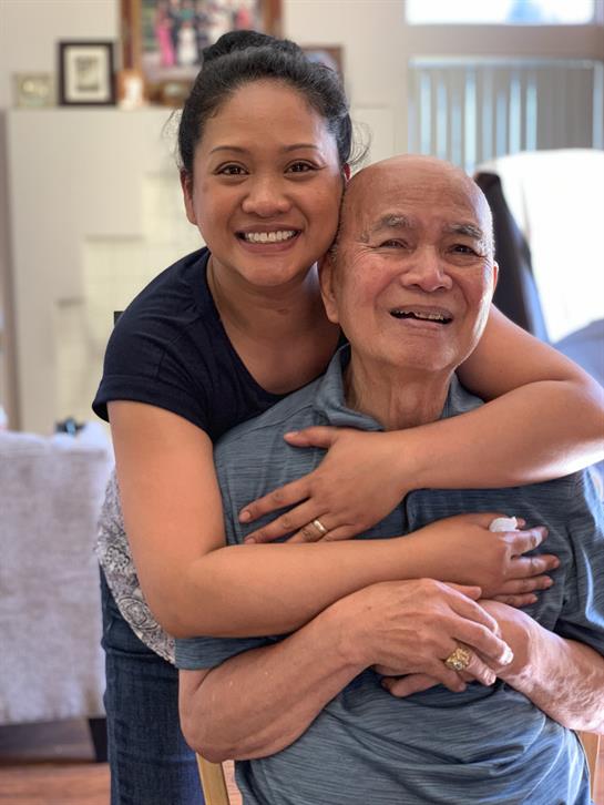 A woman hugs an elderly man from behind, both smiling joyfully in a friendly atmosphere.