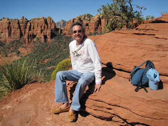 A man sits on a vibrant red rock in Sedona, basking in the sunlight amidst stunning landscapes.