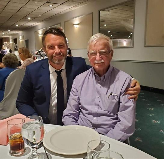 Two men enjoy each other's company while seated at a table decorated for a formal dinner.