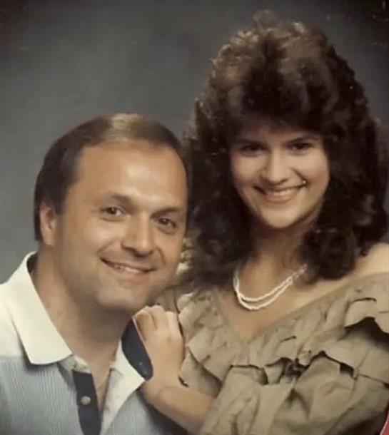 A couple smiles warmly in a studio portrait, showcasing vintage hairstyles and fashion.