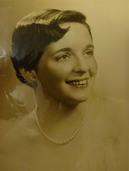 A woman smiles brightly, wearing a pearl necklace, captured in a vintage style portrait.