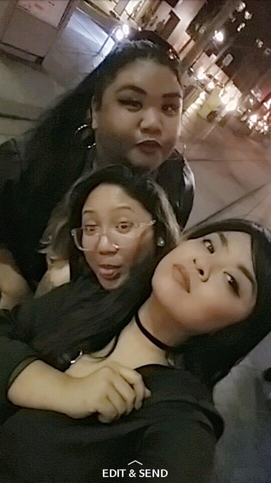 Three friends pose for a fun group selfie in a vibrant city environment at night.
