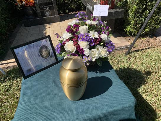 A golden urn rests on a table adorned with a floral arrangement and a framed tribute nearby.