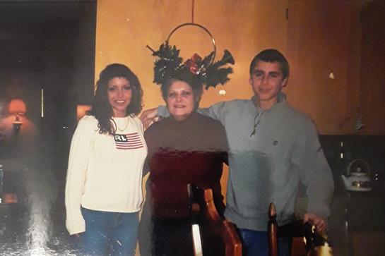 Three family members pose together, smiling warmly, in a cozy room adorned with festive decorations.