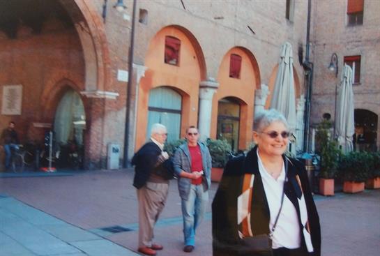 Older adults smile and converse in a vibrant square surrounded by historic architecture.