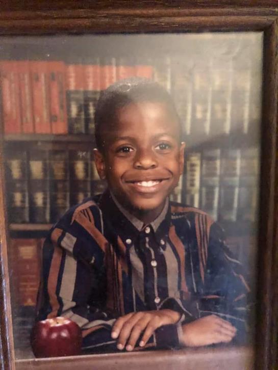 A smiling boy confidently stands before bookshelves filled with books.