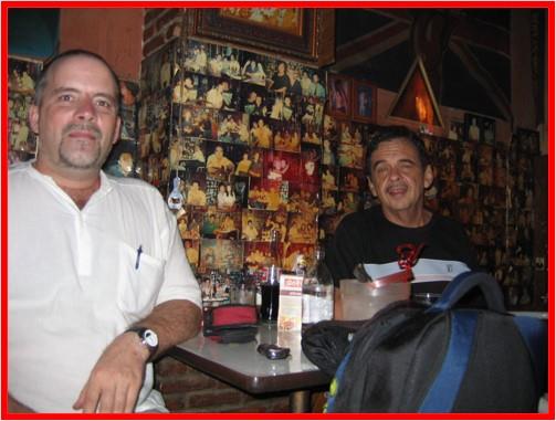 Two men sit at a table in a vibrant bar filled with photos and enjoy their drinks.